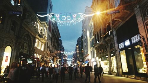 People in illuminated city against sky at night