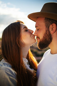 Side view of young couple kissing against sky