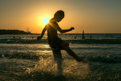 Boy kicking water in sea during sunset