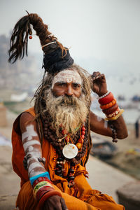 Varanasi, india - february, 2018: aged bearded hindu male in orange turban wearing red sleeveless vest standing on street and looking at camera