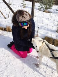 High angle view of woman in warm clothing kneeling by dog on snow covered field