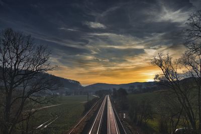 Railroad tracks by road against sky during sunset