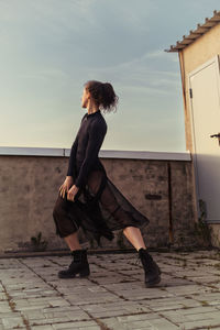 A ballerina in a black skirt and bodysuit walks on the roof admiring the sunset in the city