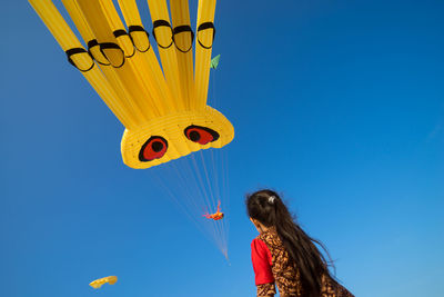 Low angle view of girl looking at kite flying against clear blue sky
