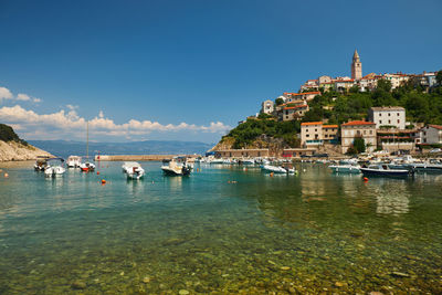 Boats in harbor by buildings against blue sky