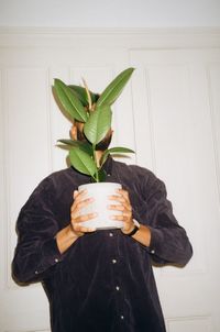 Midsection of man holding leaf against wall