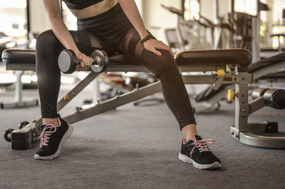 Low section of woman lifting dumbbell in gym