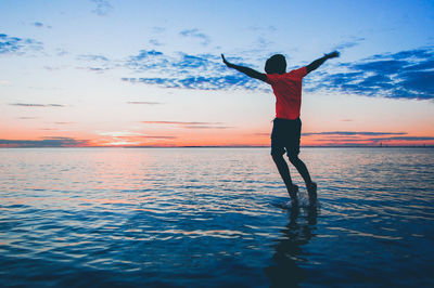 Rear view of boy in sea against sky during sunset