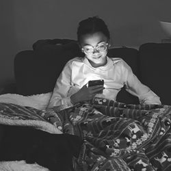 Young woman using mobile phone while relaxing on bed at home