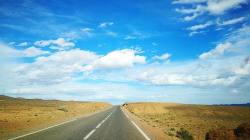 Road passing through landscape against cloudy sky