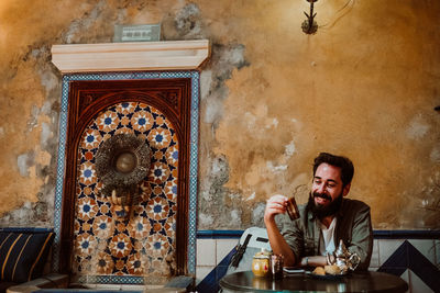 Portrait of smiling man sitting on table against wall