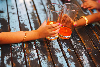 Cropped hands of girls holding glasses with drink on table