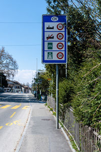 Road sign by trees in city against sky