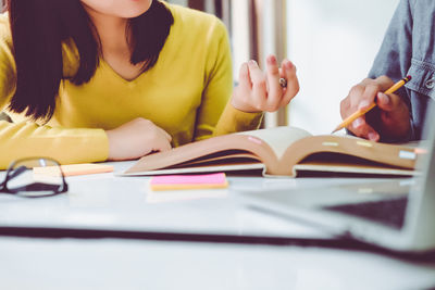 Midsection of woman reading book on table