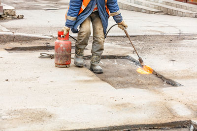 A worker using a gas burner heats the asphalt pavement for patching the road.