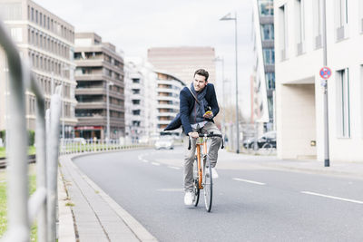 Businessman riding bicycle in the city, while using smartphone and earphones