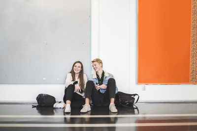 Young man sitting with female friend in corridor of university