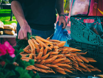 Midsection of man buying carrots in market