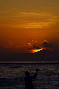 Silhouette man fishing in sea against sunset sky