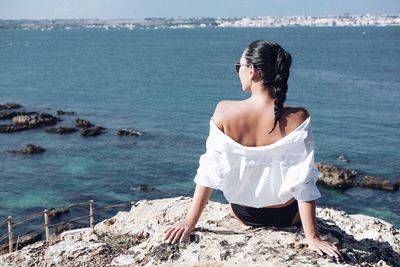 Rear view of woman sitting on cliff against sea