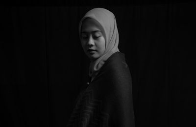 Young woman looking away while standing against black background