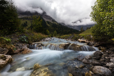 Scenic view of waterfall against cloudy sky