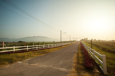 Road by electricity pylons against clear sky