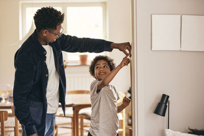 Smiling son looking at father while checking height at home