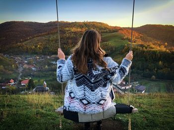Rear view of adult woman sitting on a swing on top of a hill