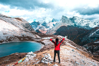 Rear view of woman standing on snowcapped mountain against sky