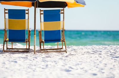 Colorful beach chairs and a beach umbrella sitting on the white sandy beach in florida