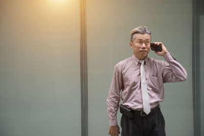 Well-dressed businessman using phone while standing against building in city 