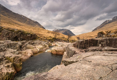 Scenic view of stream and mountains against cloudy sky