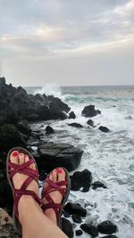 Low section of woman relaxing at beach against sky