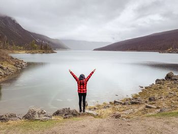 Rear view of woman standing by lake against sky