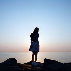 Full length of woman standing on rock by sea against sky during sunset