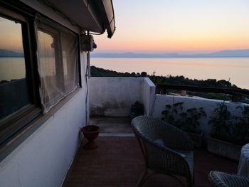 Chairs and table by sea against sky during sunset