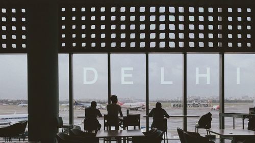 People sitting by table against window in airport