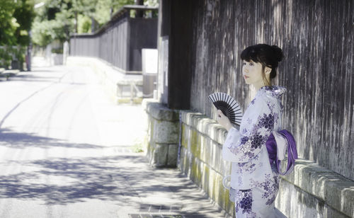 Woman in kimono holding hand fan while standing on road