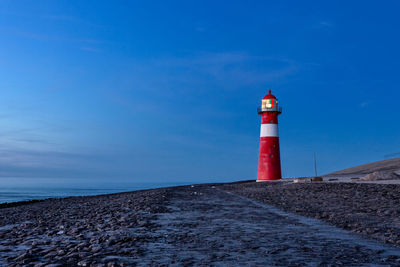 Lighthouse at sea shore against blue sky