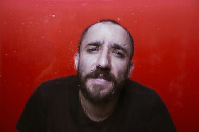 Portrait of mid adult man sitting against red wall looking through wet window