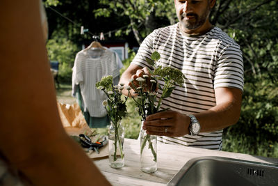 Man arranging plant in vase by sink in backyard