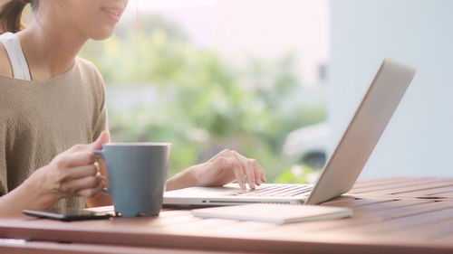 Midsection of woman holding coffee cup on table