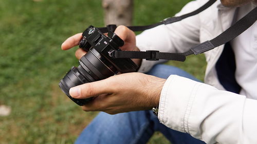 Midsection of man holding camera sitting on grass