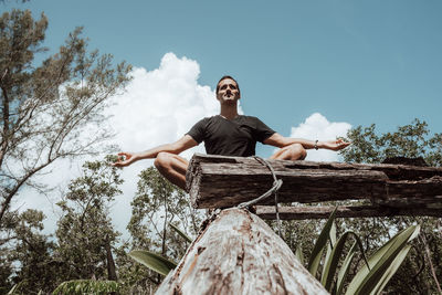 Low angle view of yoga man sitting against trees against sky