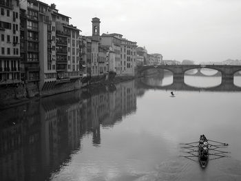 Bridge over river by buildings in city against sky