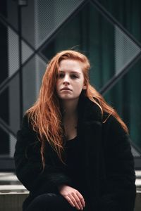Portrait of beautiful young woman sitting against building