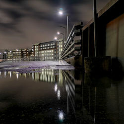 Illuminated buildings by lake against sky in city at night