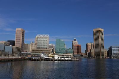 Modern buildings by river against blue sky