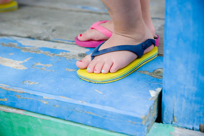 Low section of girl wearing flip-flops while standing on floorboard